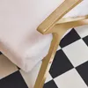 A close-up of a white armchair with a gold frame, placed on a black and white checkered floor. Produktbild-Vorschau