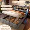 A grey upholstered bed with its storage compartments open, revealing folded linens and other items. The headboard has shelves and integrated lighting. Náhľad obrázku produktu