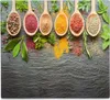 Wooden spoons filled with various spices and herbs are arranged on a dark slate surface, with some spices spilled around them. Podgląd zdjęcia produktu