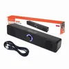 A black computer soundbar speaker and its charging cable are displayed on a white background, with the product's packaging visible in the background. Voir les images du produit