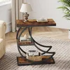 A bedside table with a lamp, books, and a basket is placed on a rug next to a sofa. Produktbild-Vorschau
