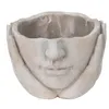 A close-up, front-facing view of a decorative planter shaped like a face with hands supporting the head. Náhled obrázku produktu