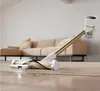 A cordless vacuum cleaner is shown in use on a carpeted floor with a sofa in the background. Podgląd zdjęcia produktu