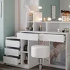 A white vanity table with drawers and shelves, a white stool, and various makeup products and accessories. Voir les images du produit