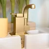 A close-up shot of a golden kitchen faucet with a yellow cup to the left and a white sink basin. Podgląd zdjęcia produktu