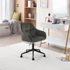 A dark gray velvet office chair with a black base is placed on a white rug in a room with a vanity desk and shelves. Produktbild-Vorschau