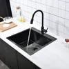 A black kitchen sink with a black faucet with water running into it, on a white marble countertop with a tiled backsplash. Náhled obrázku produktu