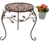 A metal plant stand with a decorative bird and leaf motif, next to a potted plant in a metal bucket. Produktbild-Vorschau