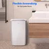 A white dehumidifier is placed on a tiled floor next to a bathroom vanity with a sink. The scene is clean and modern. Produktbild-Vorschau