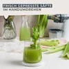 A glass of fresh green juice with celery stalks next to it, and a juicer in the background. Produktbild-Vorschau