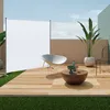 An outdoor patio scene with a white screen, a chair, a coffee table with decorative items, and a potted plant. Produktbild-Vorschau
