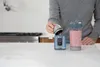 A person is pouring liquid into a portable blender base, with a filled blender cup next to it. Podgląd zdjęcia produktu