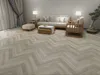 A living room with a sofa, coffee table, armchair, and a bonsai tree, showcasing the herringbone flooring. Produktbild-Vorschau