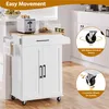 A white kitchen cart with a wooden top is shown in a kitchen setting. The cart has two doors, a drawer, and wheels. There is a toaster and some bread on the top surface. Inset images highlight the wheels. Produktbild-Vorschau