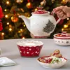 A Christmas-themed tea set and cookies are arranged on a table, with a decorated Christmas tree in the background. Náhled obrázku produktu