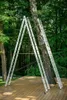 Two ladders are set up in an A-frame configuration next to a tree on a wooden deck, surrounded by greenery. Náhľad obrázku produktu