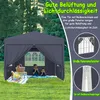 A dark gray pop-up tent set up on a grassy lawn, with two children eating watermelon inside. There are picnic items in front of the tent. Produktbild-Vorschau
