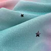 A close-up view of a fabric with a gradient color scheme and star cutouts. Voir les images du produit