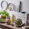 A collection of ceramic tableware and fresh produce displayed on a wooden table and shelf. Produktbild-Vorschau