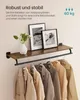 A wall-mounted shelf with a hanging rod, displaying framed pictures and a vase on the shelf, and several coats hanging from the rod. Produktbild-Vorschau