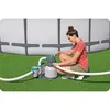 A woman is adjusting a sand filter pump next to an above-ground swimming pool. Produktbild-Vorschau