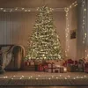 A Christmas tree decorated with warm white LED lights, surrounded by gifts and a teddy bear in a cozy room setting. Produktbild-Vorschau