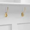 A close-up view of two gold coat hooks mounted on a white wall, beneath a white shelf. Produktbild-Vorschau