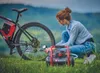 A woman is using a portable air compressor to inflate a bicycle tire outdoors. Anteprima dell’immagine prodotto