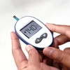 A person's hands are holding a digital glucose meter with a test strip inserted. The meter displays a reading of 140 mg/dL. Anteprima dell’immagine prodotto