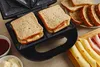 A sandwich maker with two sandwiches inside, along with ingredients for making sandwiches. Náhľad obrázku produktu