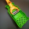 A close-up shot of a green and orange vegetable peeler with a silver blade. Voir les images du produit