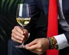 A person in a suit holding a glass of white wine. Produktbild-Vorschau