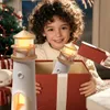 A child is opening a gift box containing two lighthouse-shaped lamps, with a Christmas tree in the background. Produktbild-Vorschau