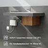 A white mini water heater is mounted on a gray wall below a sink, with a wooden cabinet underneath. Produktbild-Vorschau
