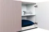 The image shows the inside of a cabinet with shelves. On the shelves are plates and a pillow. Podgląd zdjęcia produktu