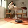 A woman is preparing coffee at a dining table while a robot vacuum cleans the floor. Náhled obrázku produktu