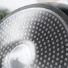 A close-up view of the textured bottom of a black frying pan with a silver metallic finish and a pattern of raised dots. Produktbild-Vorschau