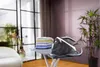 A modern steam iron station on an ironing board, with folded clothes and a vase of flowers in the background. A potted plant is also visible. Voir les images du produit