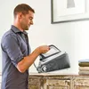 A man is holding a steam iron over a wooden dresser. Voir les images du produit