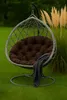 A hanging egg chair with a brown cushion and a gray blanket draped over it, set on a green lawn with tall, tan grasses in the background. Voir les images du produit