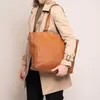 A person wearing a trench coat and holding a brown leather tote bag. Voir les images du produit