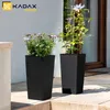 Two tall black planters with plants are placed on a patio next to a building. Anteprima dell’immagine prodotto