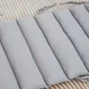 A close-up view of a padded bumper or cushion, likely for a baby's crib or playpen, lying on a striped fabric background. Produktbild-Vorschau