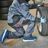 A person in work clothes is kneeling and changing a car tire. Produktbild-Vorschau