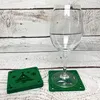 A wine glass sits on a green coaster with a Christmas tree design, next to a stack of similar coasters. Produktbild-Vorschau