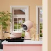 A pink mini range hood is placed on a kitchen counter next to a pot on an induction cooktop, with a plant and windows in the background. Náhľad obrázku produktu