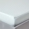 A close-up view of a striped fitted sheet on a bed. Náhled obrázku produktu