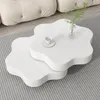 A modern living room scene with a white, flower-shaped coffee table set on a striped rug in front of a tufted sofa. Voir les images du produit