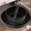 A set of black pots and pans stacked inside a wooden drawer. Produktbild-Vorschau