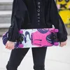 A person holding a skateboard with a colorful graphic design. Voir les images du produit